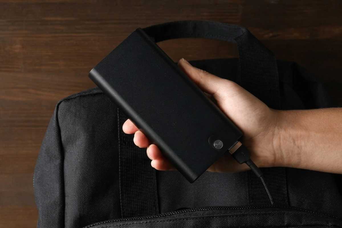 Prenosivi power bank uređaj u ruci pored poslovnog ranca kao praktičan tech korporativni poklon